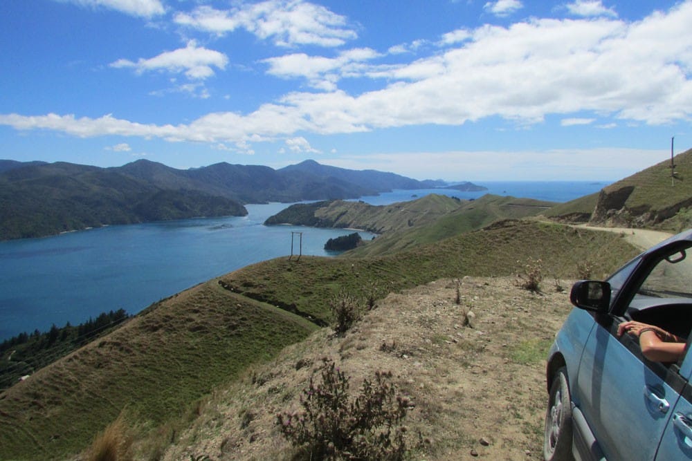 Viajar por Nueva Zelanda coche parado en una montaña y de fondo el lago y el cielo despejado